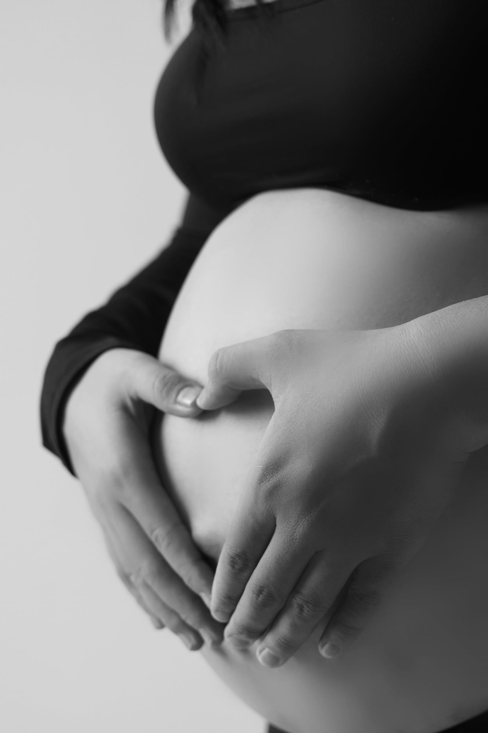 Mãos em forma de coração sobre a barriga, a preto e branco.
