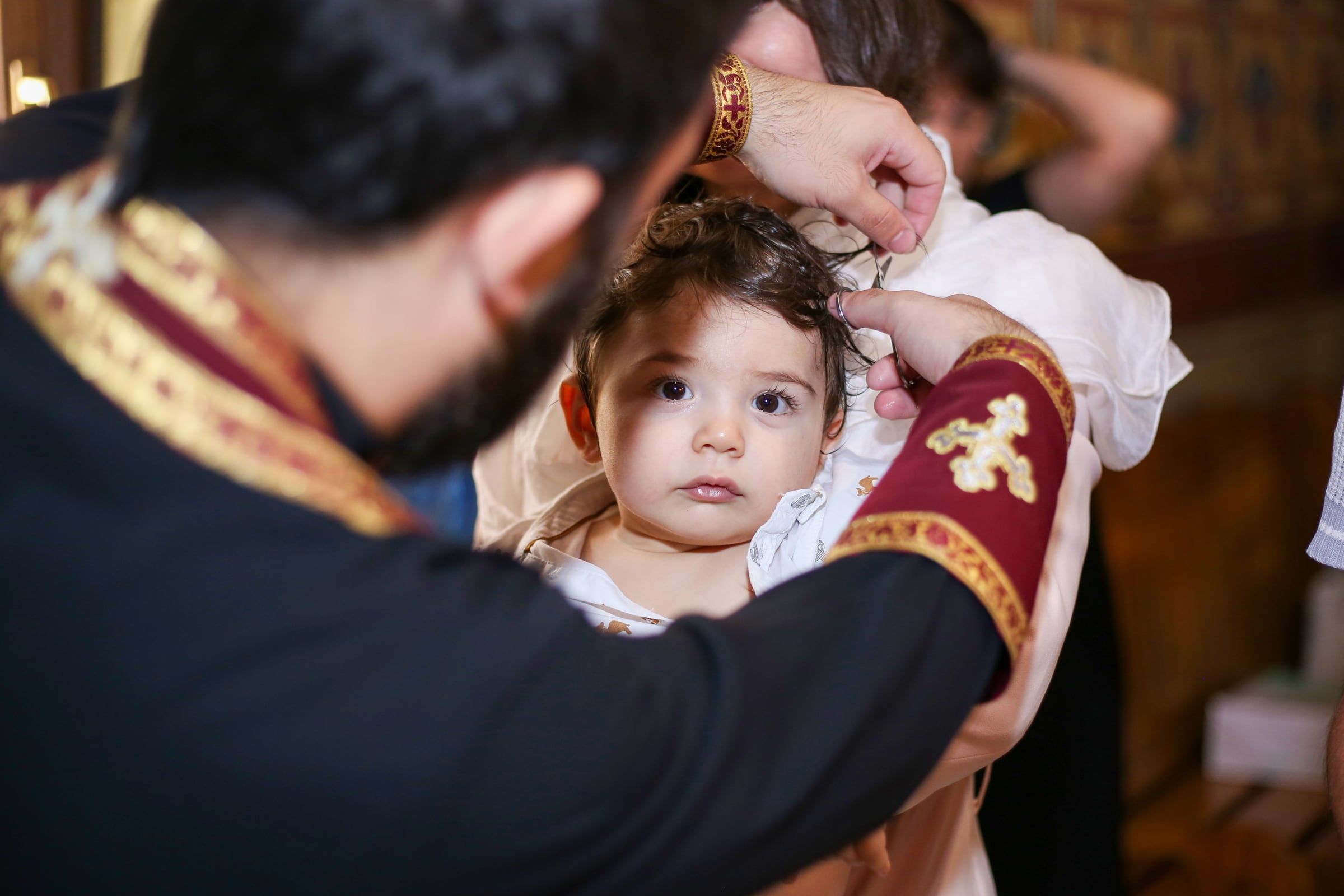 O padre segura o rosto do bebé, que olha para a câmara.