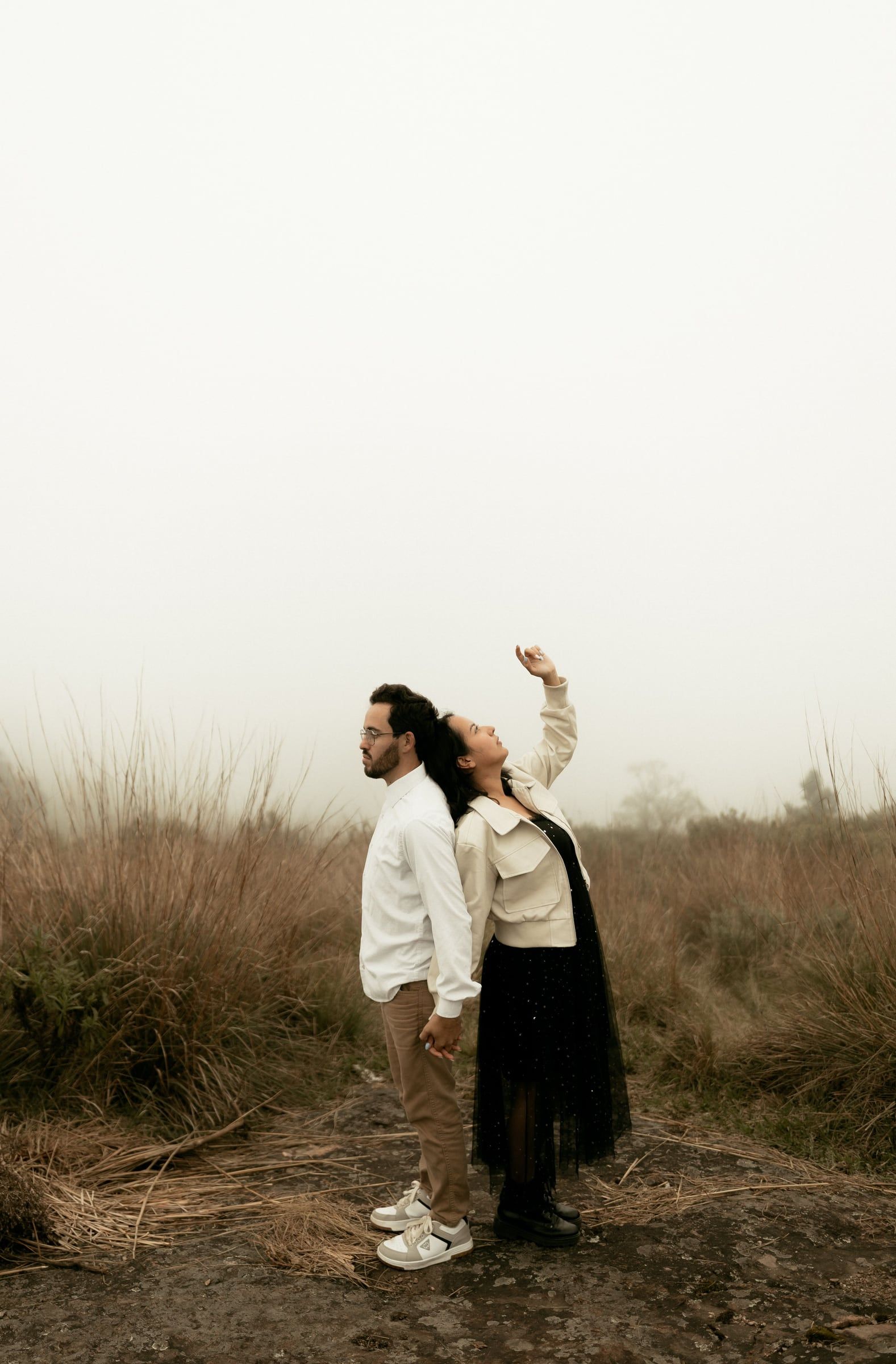 Casal ao longe num campo seco, ela de braço no ar a apontar qualquer coisa.